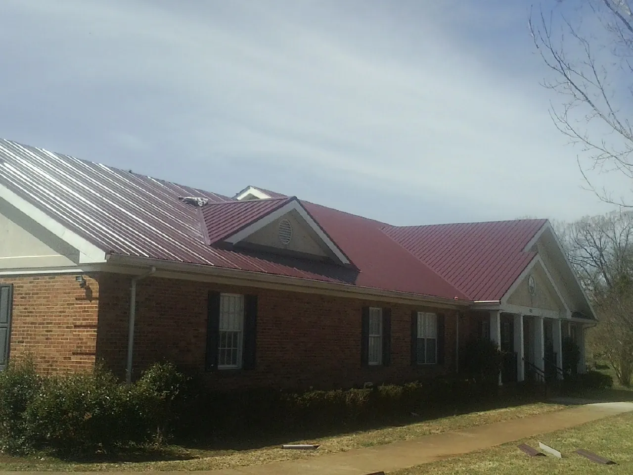 Red metal roof with gabled entries on a long brick building, from a Hail Damage Roof Repair job in Woodbridge