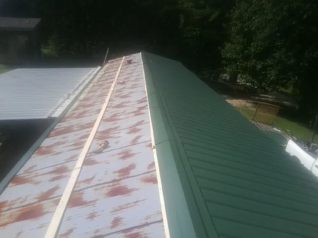 Old rusted panels beside newly installed green metal roofing in Woodbridge